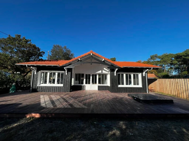Maison de plain-pied à bardage sombre, toiture en tuiles et terrasse en bois