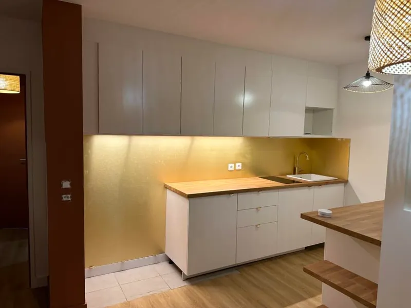 Cuisine contemporaine avec façades blanches, plans en bois, crédence ocre et suspensions tressées