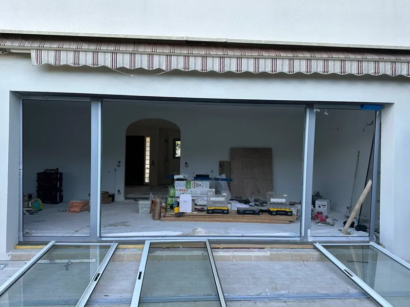 Installation en cours d’une grande baie vitrée coulissante sur la façade d’une maison avec matériaux et outils visibles