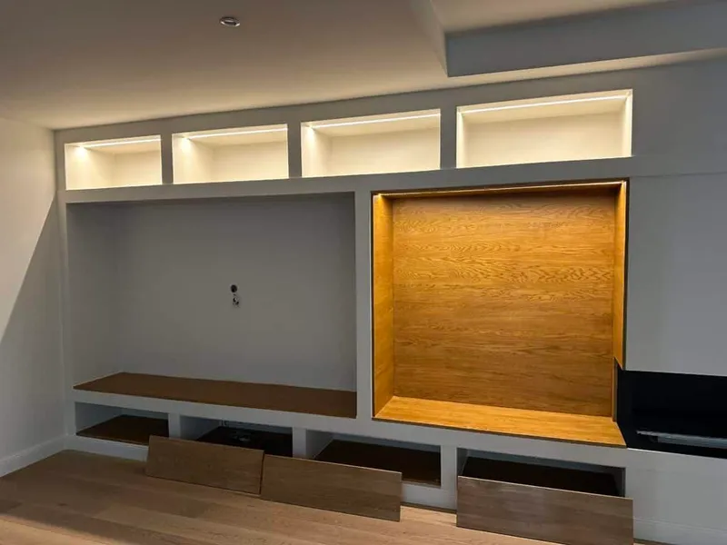 Bibliothèque terminée avec niches éclairées, inserts en bois et rangements bas autour de la cheminée