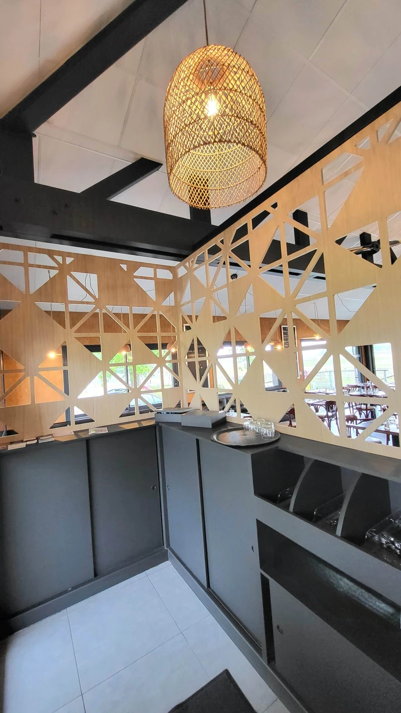 Agencement de restaurant avec claustra géométrique en bois, comptoir sombre et suspension en rotin