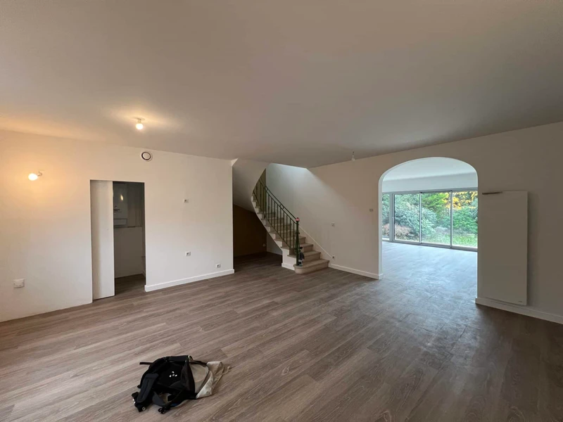 Intérieur rénové avec parquet imitation bois, escalier central et grande baie vitrée