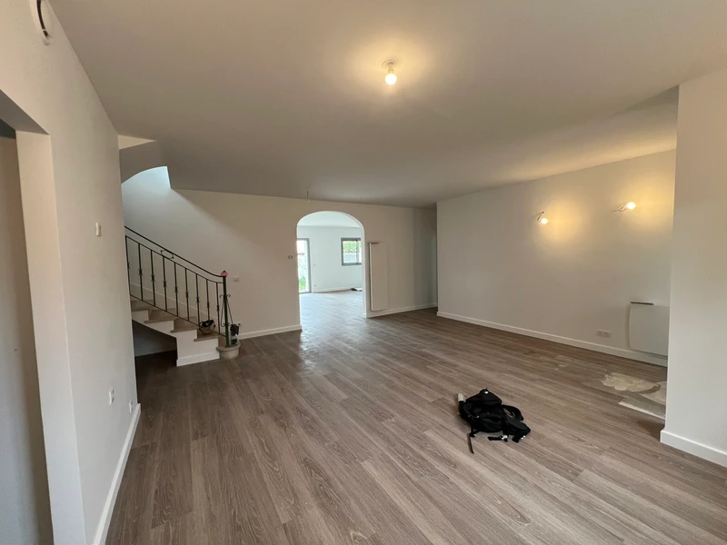 Intérieur rénové avec sol aspect bois, escalier central et ouverture vers le jardin