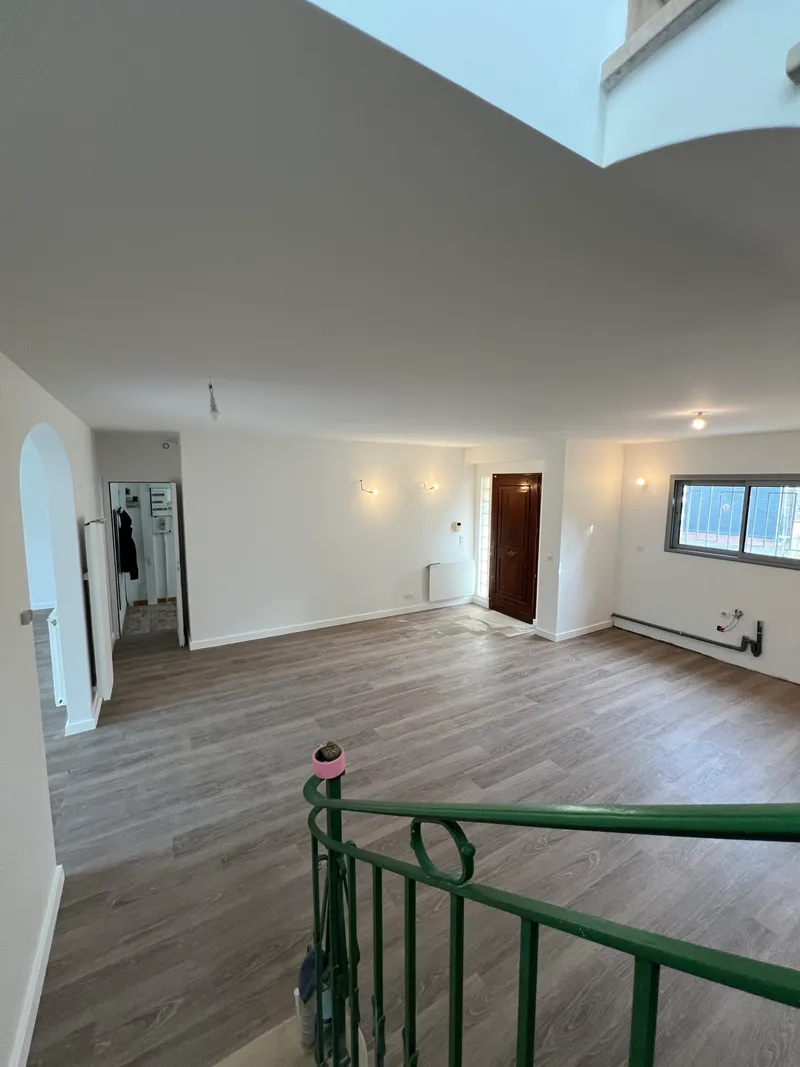 Pièce rénovée avec sol imitation parquet, murs blancs et rampe d’escalier verte
