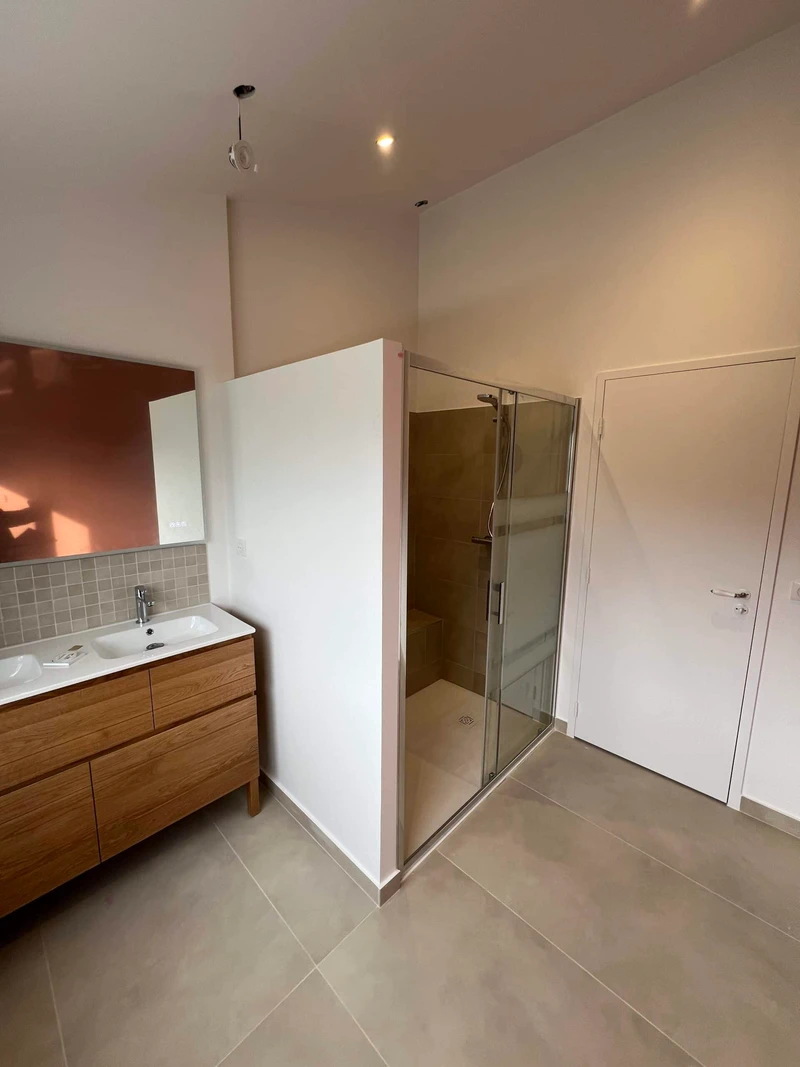 Rénovation intérieure d’une salle de bain avec douche à l’italienne, meuble vasque en bois et carrelage beige