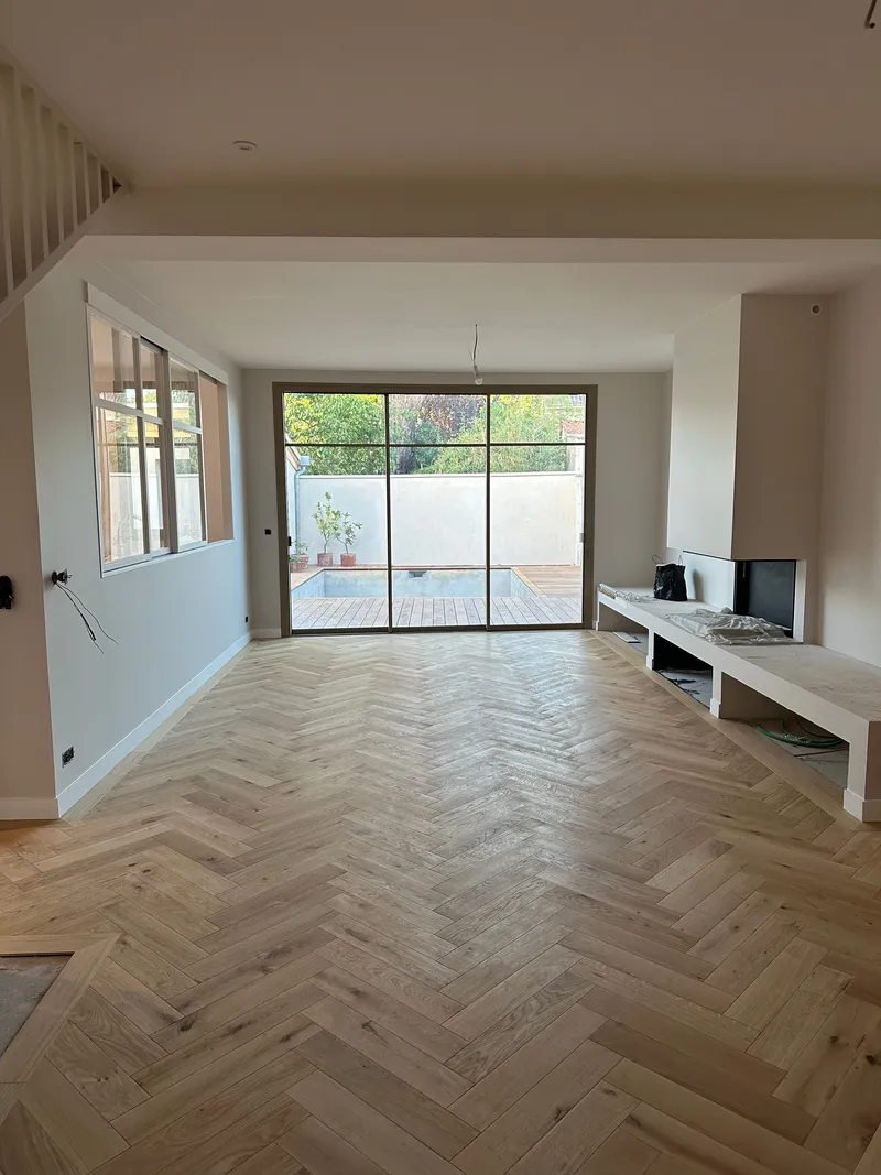 Séjour rénové avec parquet en chevrons, cheminée intégrée et grande baie vitrée