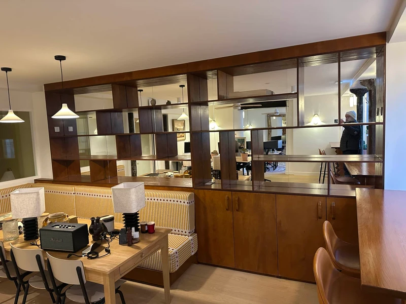 Cloison ajourée en bois sombre et miroirs séparant une salle à manger d’un bureau