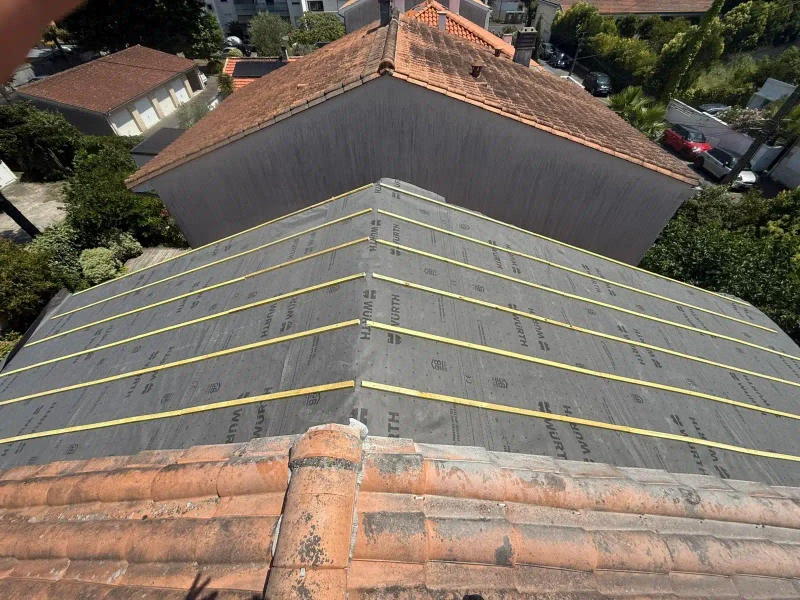 Toiture en tuiles avec écran sous-toiture gris et liteaux jaunes pendant les travaux